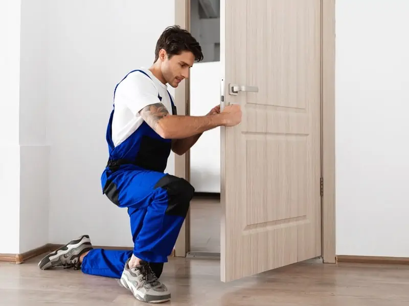 Låssmed som står på knä och jobbar med lås på en dörr.