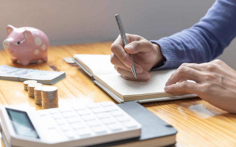 En person sitter vid skrivbord och räknar på ekonomiska kalkyler med miniräknare, papper och penna